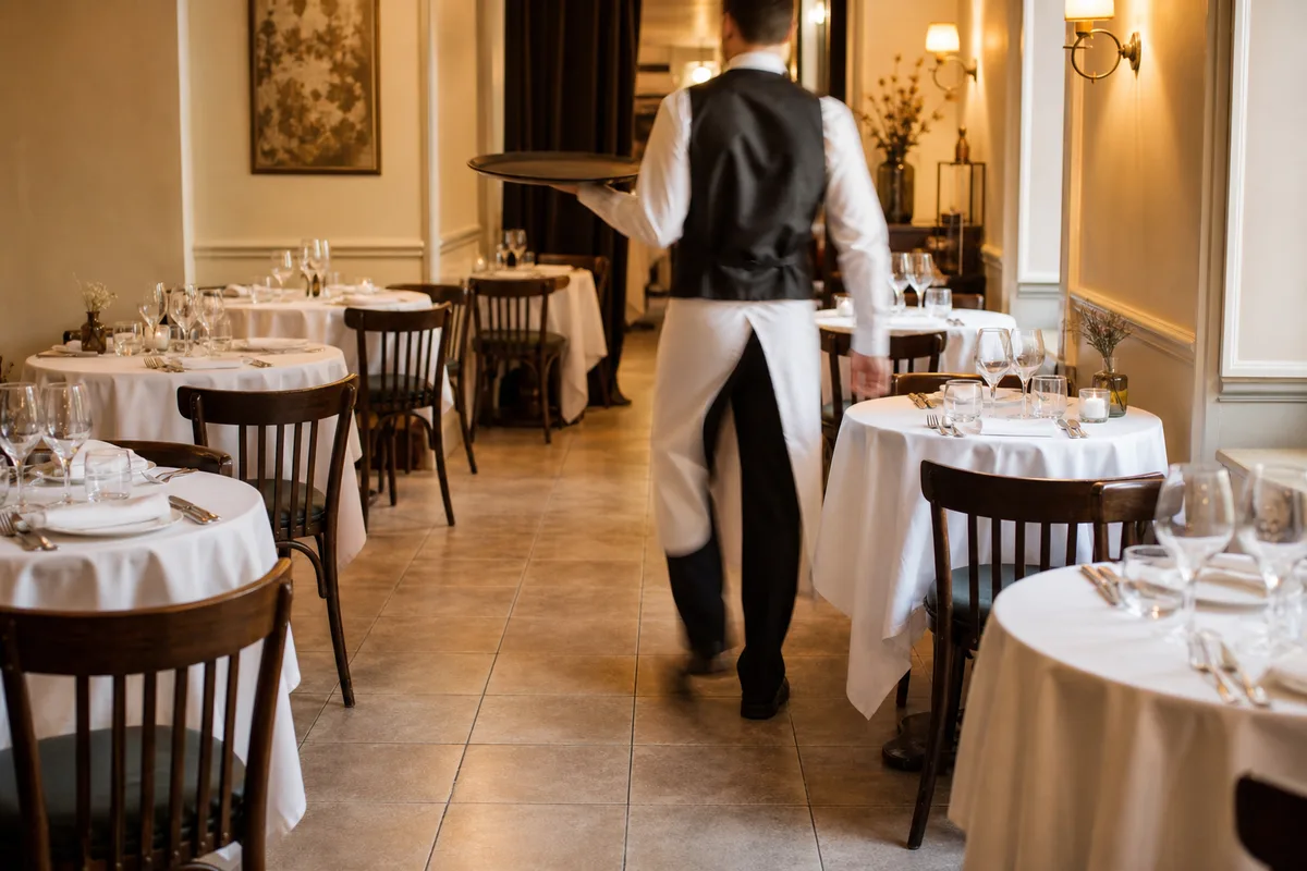 Serveur circulant entre des tables dressées dans une salle de restaurant compacte